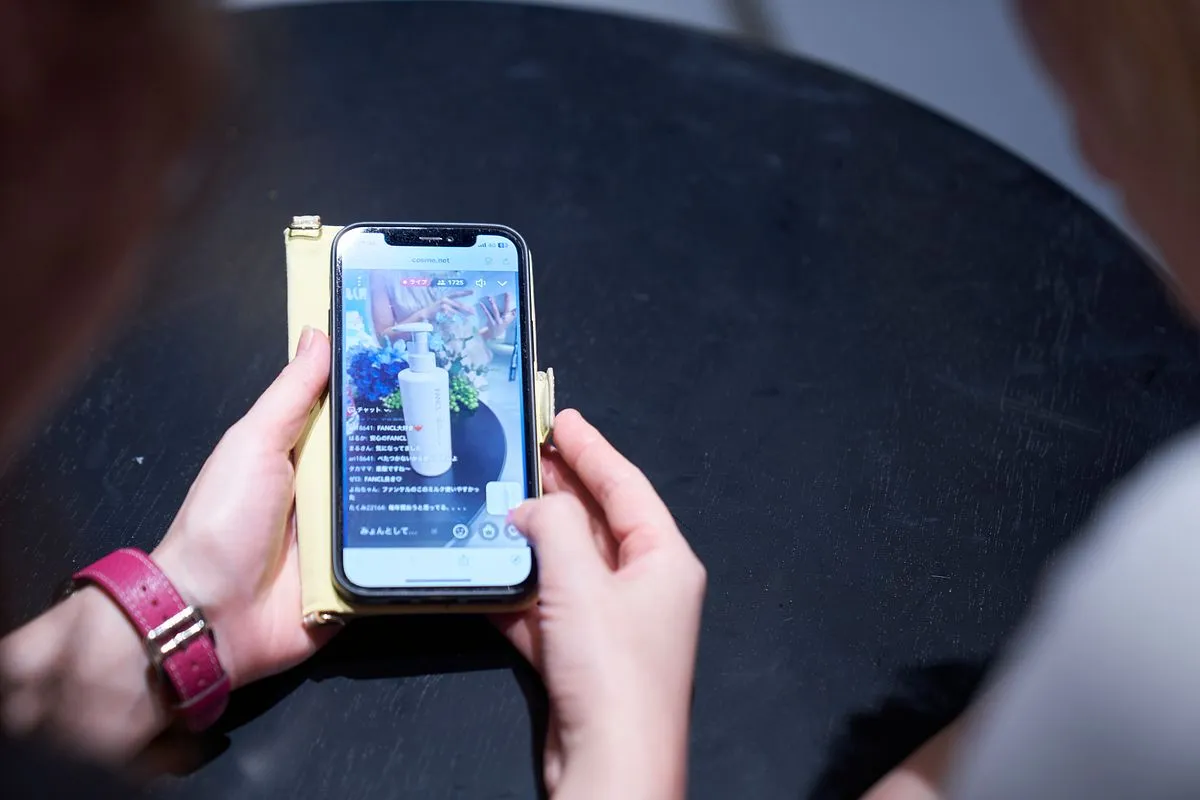 A hand holding a phone showing a live stream with chat messages over the video.
